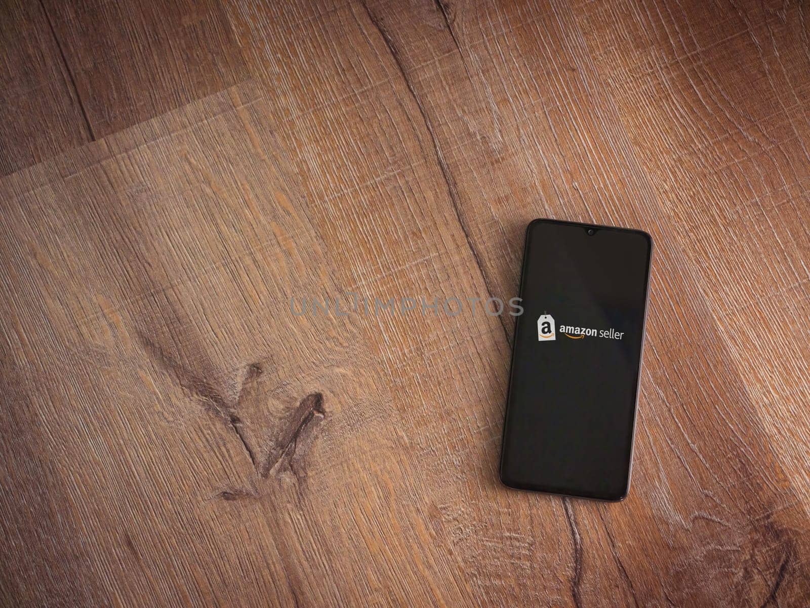 Lod, Israel - July 16,2023: Amazon Seller app launch screen on smartphone on wooden background. Top view flat lay with copy space.