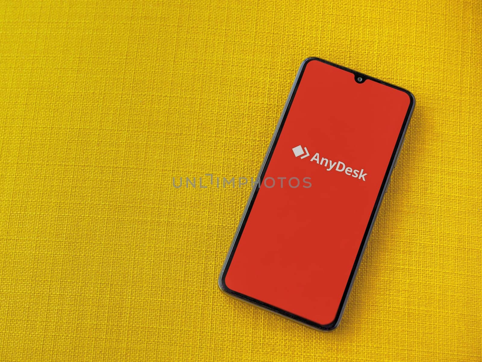 Lod, Israel - July 16,2023: Anydesk app launch screen on smartphone on yellow fabric background. Top view flat lay with copy space.