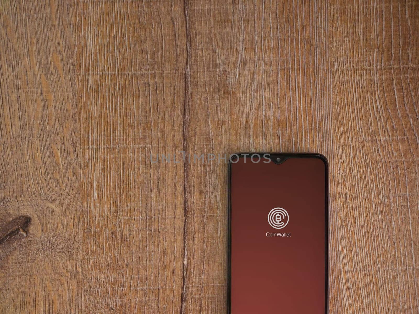 Lod, Israel - July 16,2023: CoinWallet app launch screen on smartphone on wooden background. Top view flat lay with copy space.