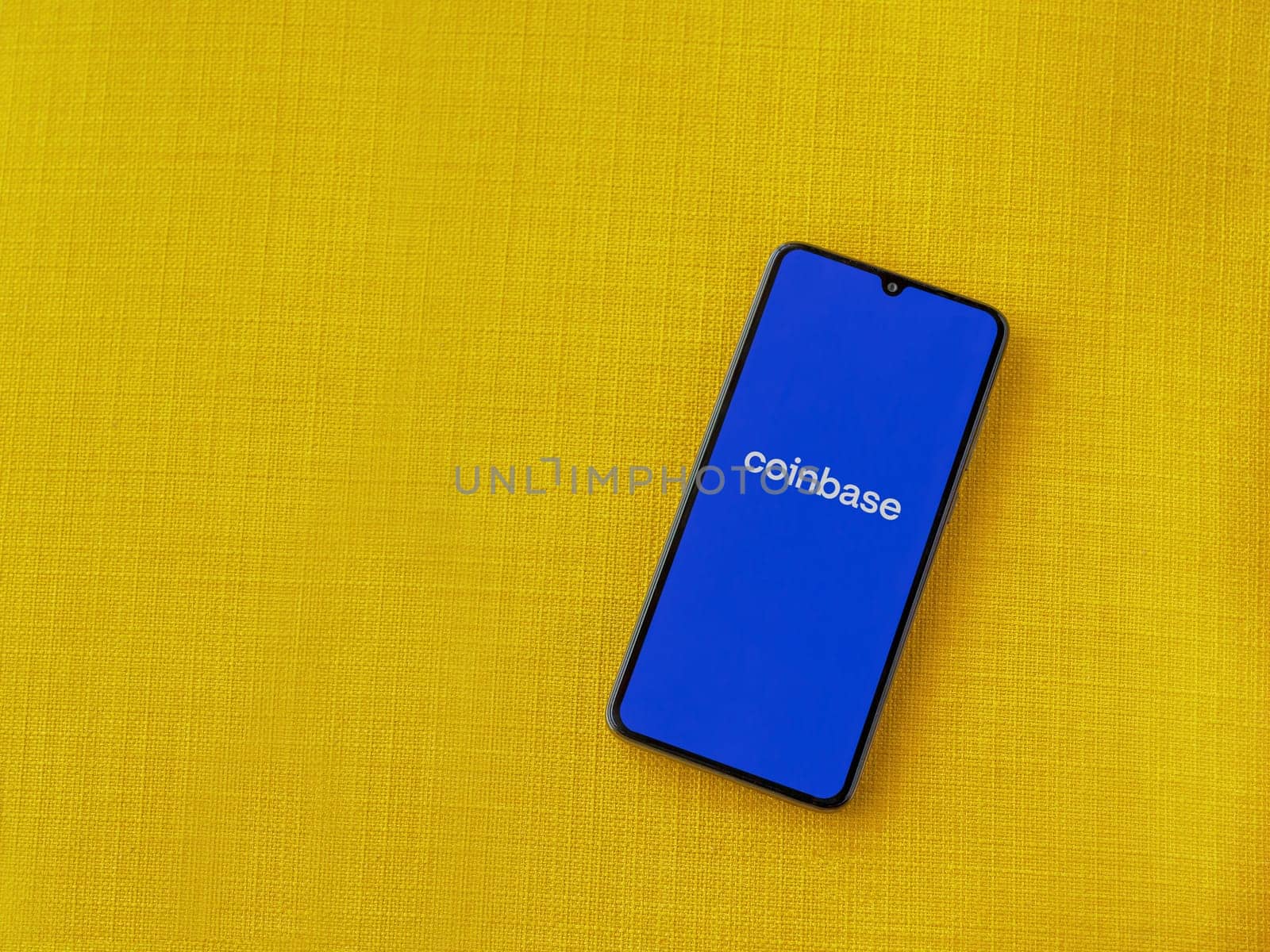 Lod, Israel - July 16,2023: Coinbase app launch screen on smartphone on yellow fabric background. Top view flat lay with copy space.