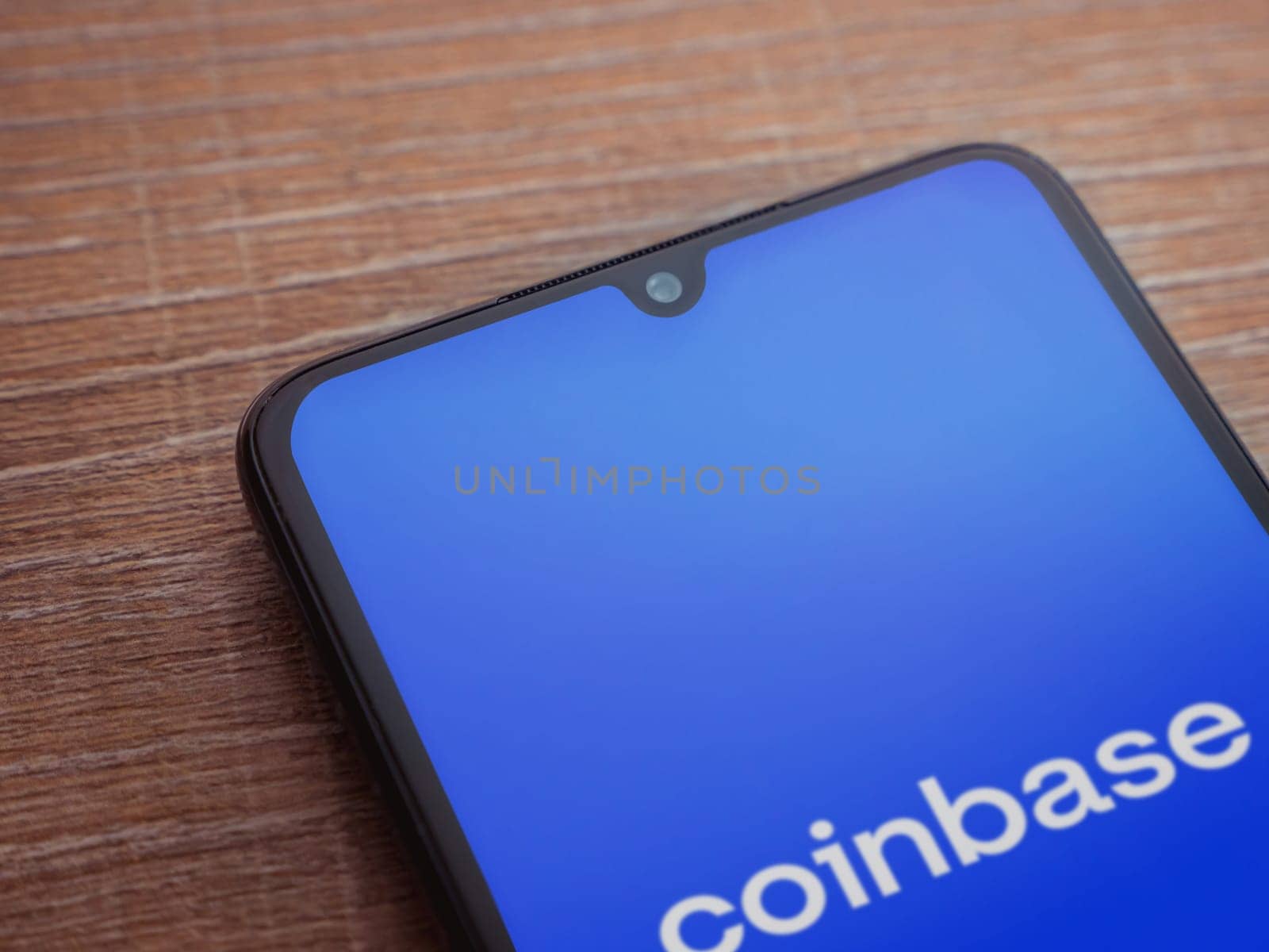 Lod, Israel - July 16,2023: Coinbase app launch screen on smartphone on wooden background. Top view flat lay with copy space.