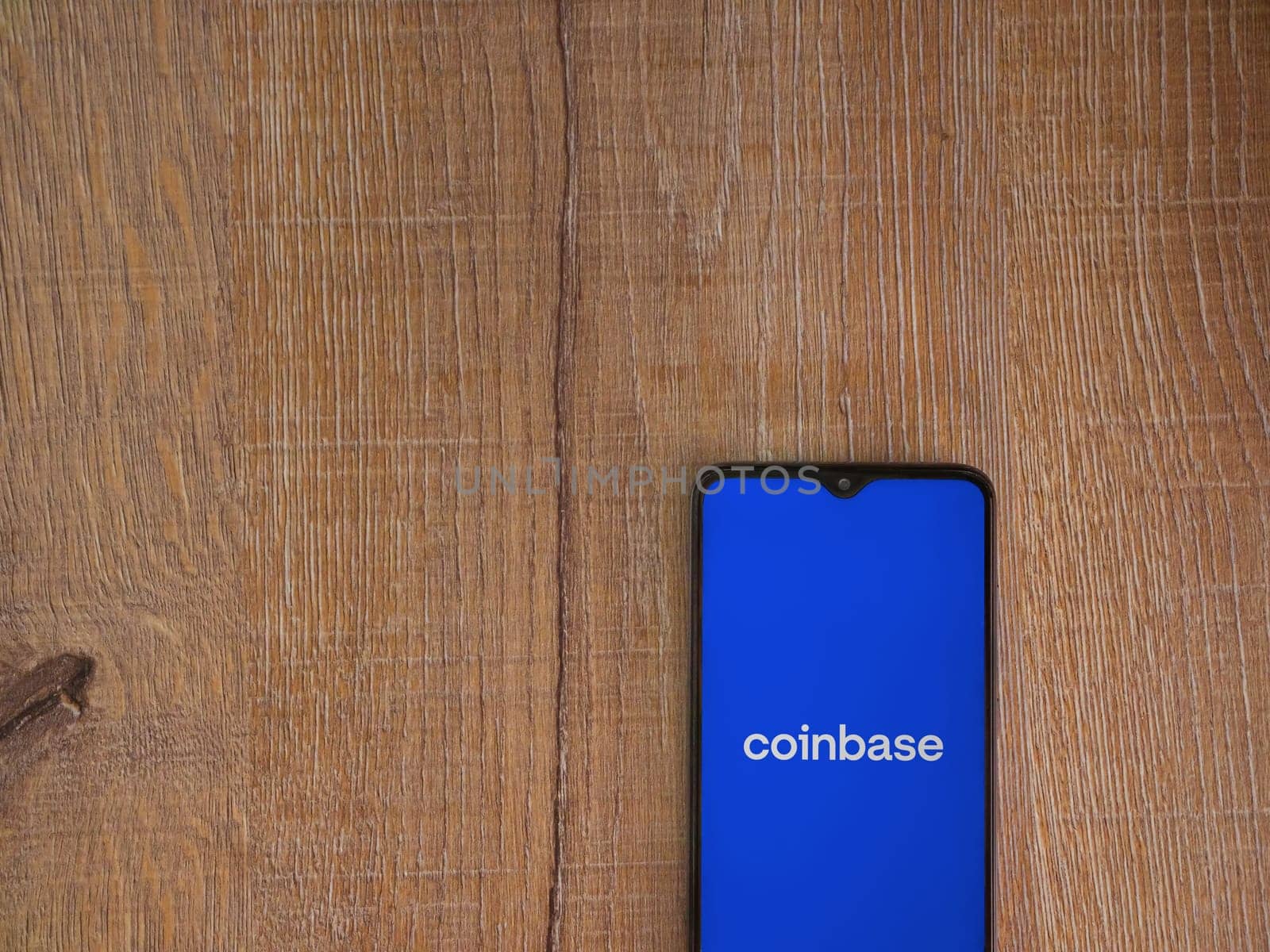 Lod, Israel - July 16,2023: Coinbase app launch screen on smartphone on wooden background. Top view flat lay with copy space.