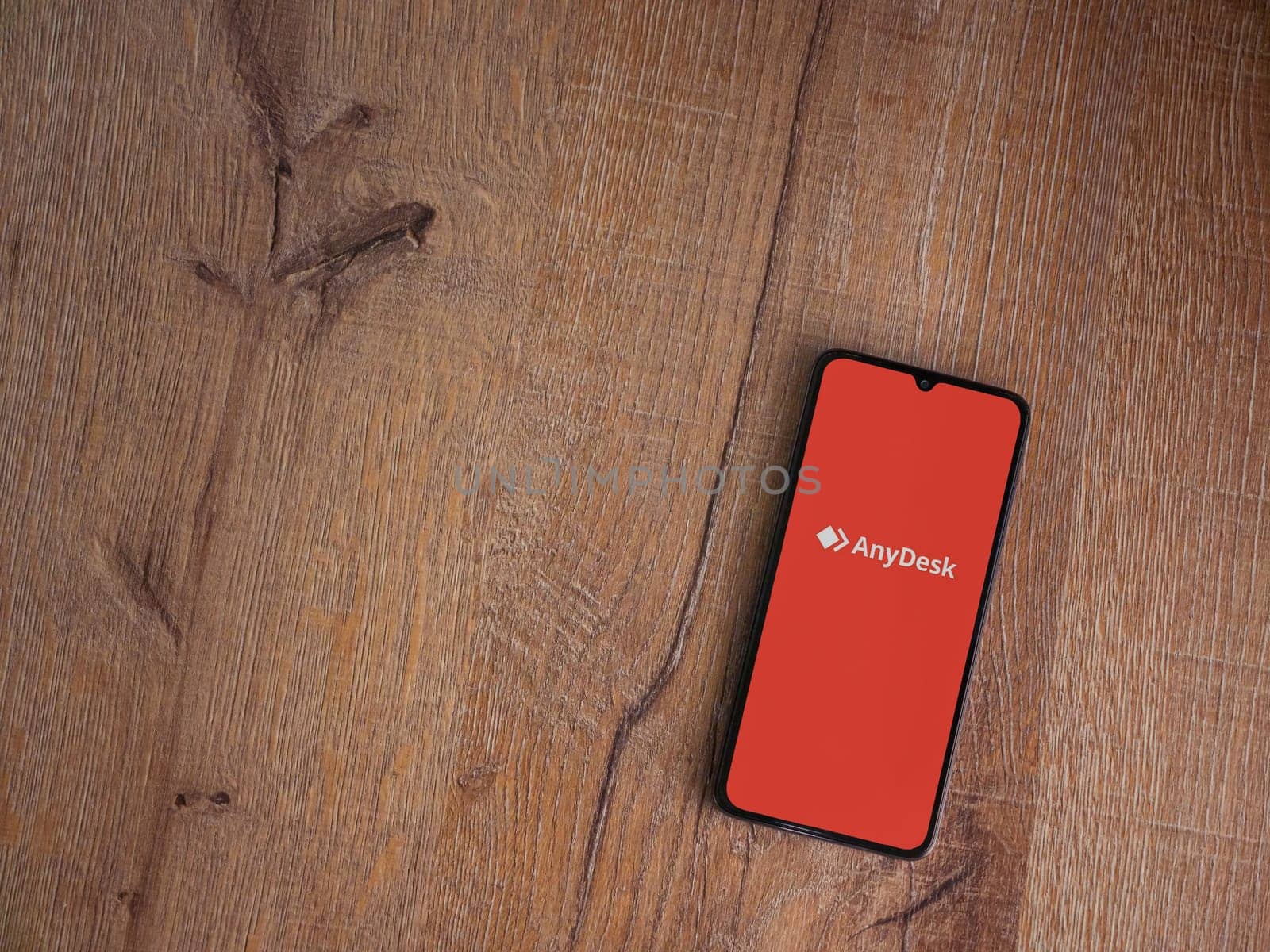 Lod, Israel - July 16,2023: Anydesk app launch screen on smartphone on wooden background. Top view flat lay with copy space.