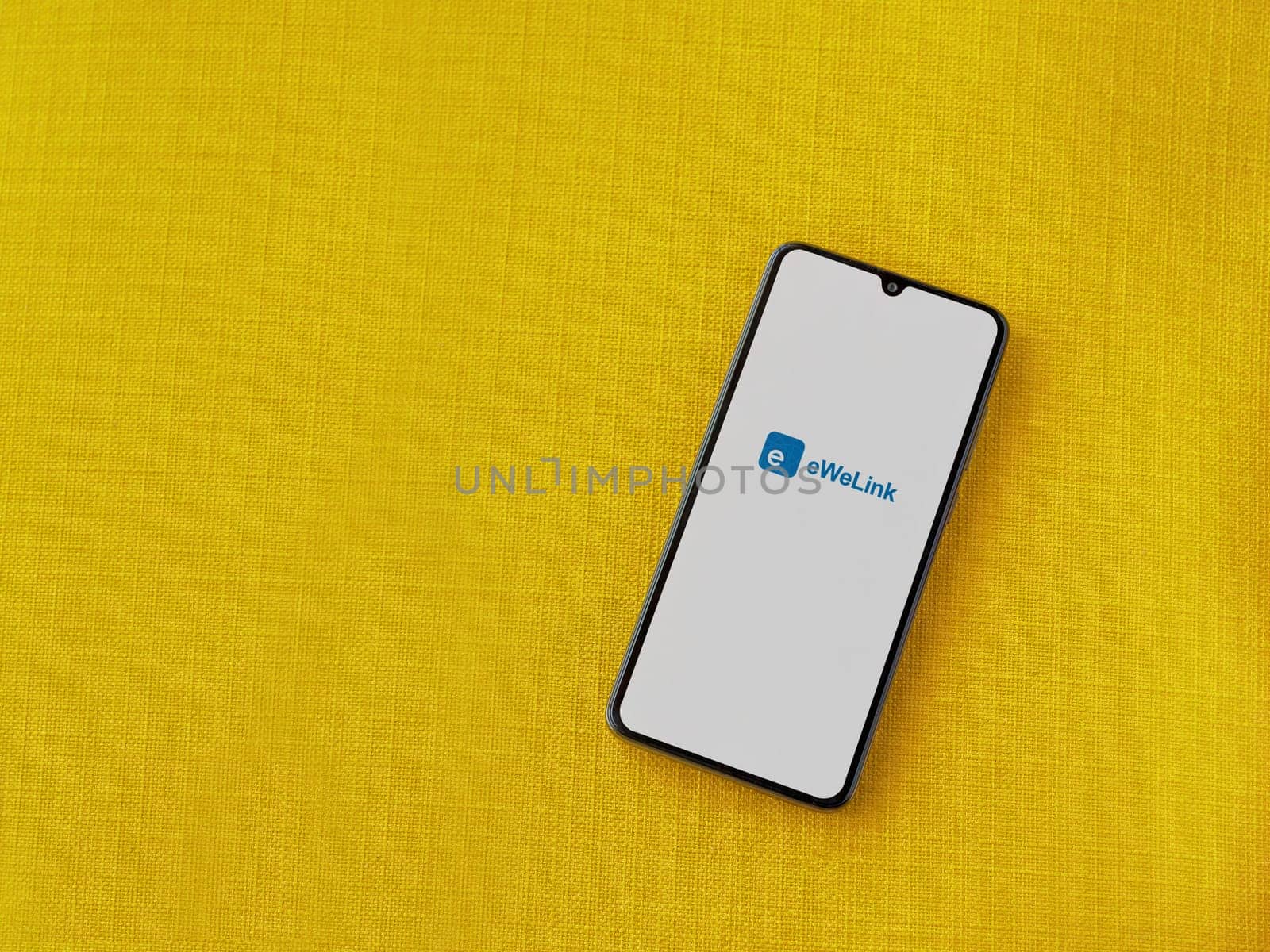 Lod, Israel - July 16,2023: eWeLink app launch screen on smartphone on yellow fabric background. Top view flat lay with copy space.
