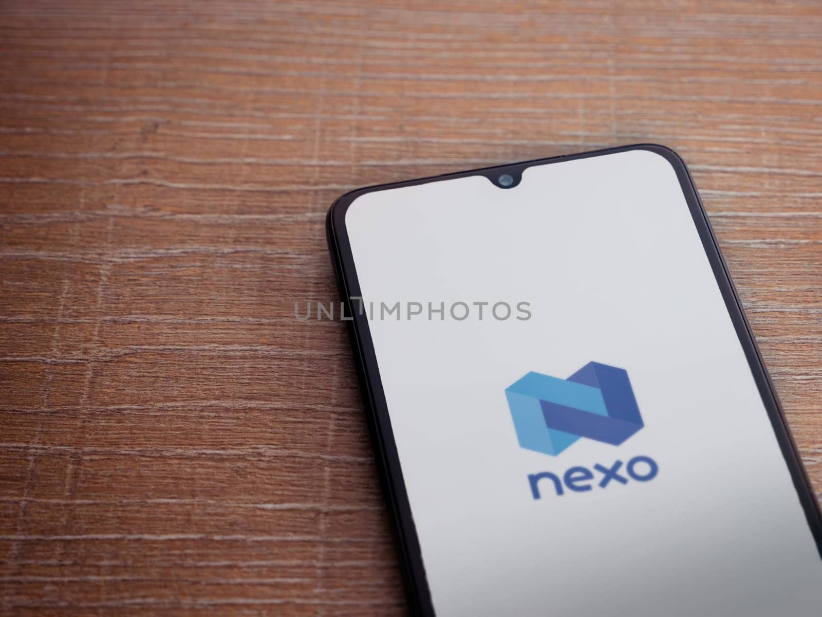 Lod, Israel - July 16,2023: Nexo app launch screen on smartphone on wooden background. Top view flat lay with copy space.