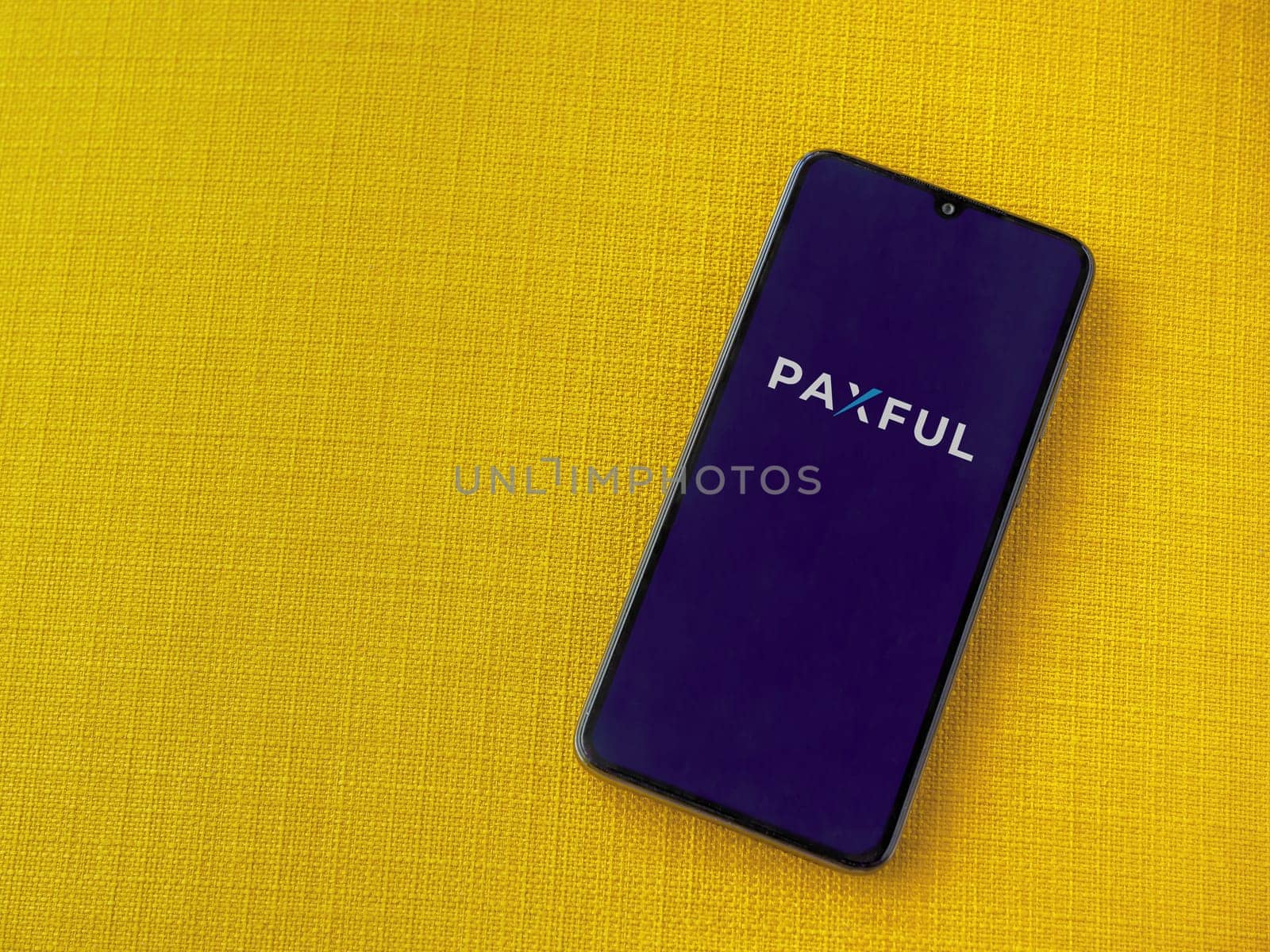 Lod, Israel - July 16,2023: Paxful app launch screen on smartphone on yellow fabric background. Top view flat lay with copy space.