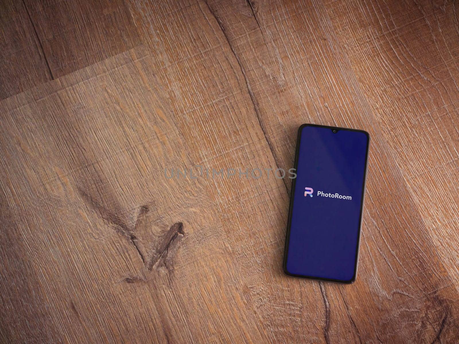 Lod, Israel - July 16,2023: PhotoRoom Studio Photo Editor app launch screen on smartphone on wooden background. Top view flat lay with copy space.