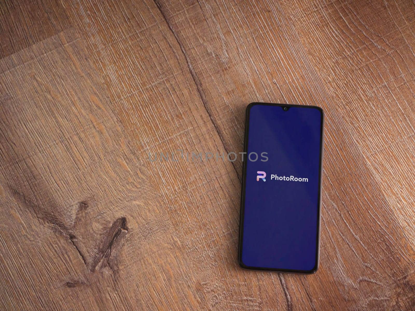 Lod, Israel - July 16,2023: PhotoRoom Studio Photo Editor app launch screen on smartphone on wooden background.. Top view flat lay with copy space.