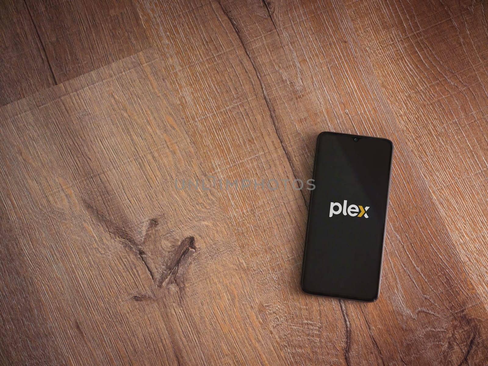 Lod, Israel - July 16,2023: Plex app launch screen on smartphone on wooden background. Top view flat lay with copy space.