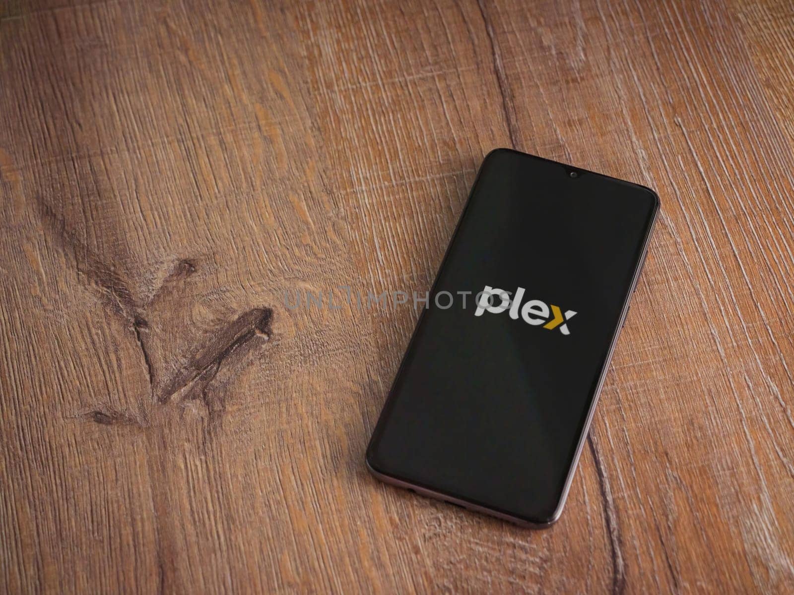 Lod, Israel - July 16,2023: Plex app launch screen on smartphone on wooden background. Top view flat lay with copy space.
