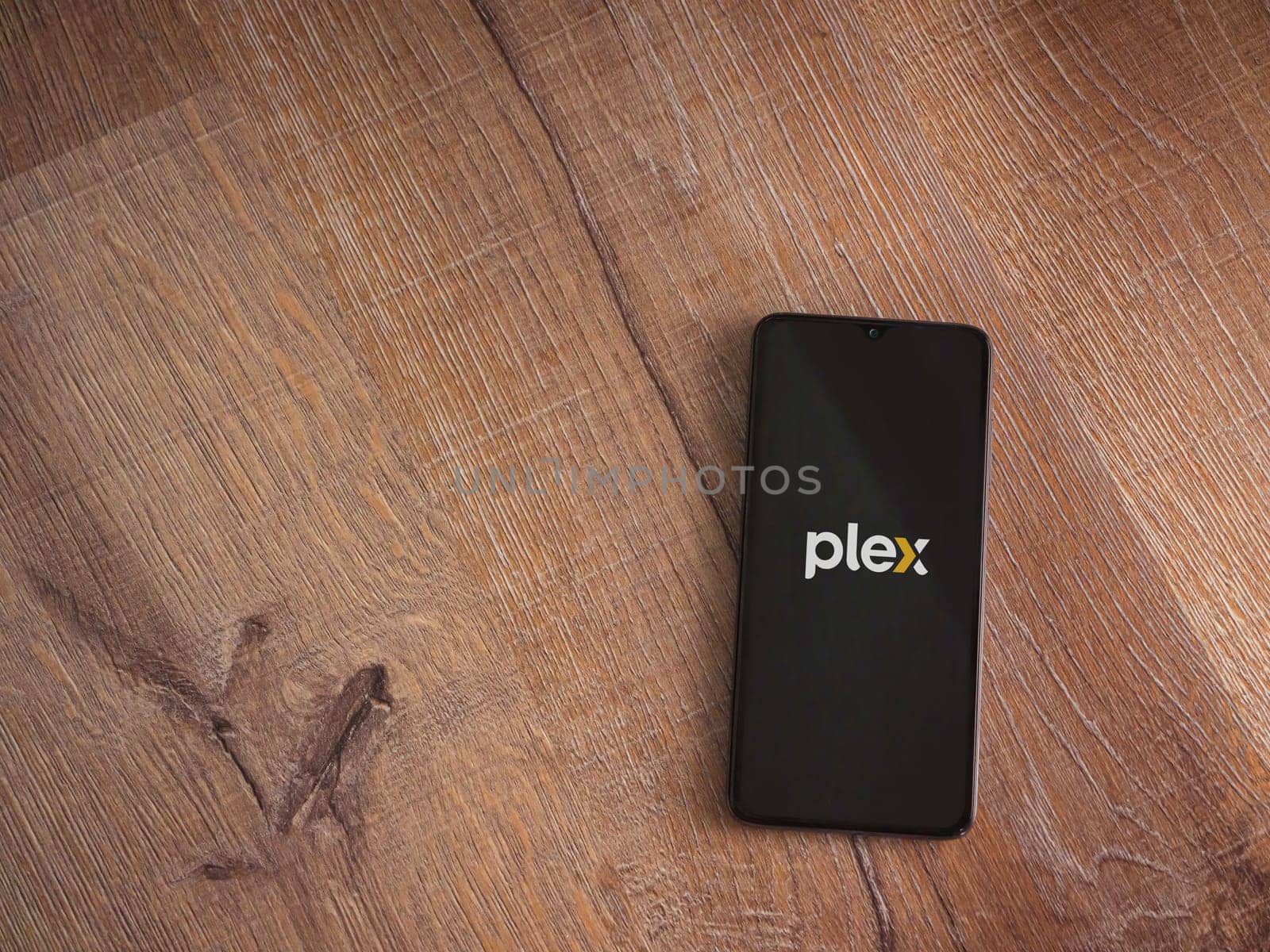 Lod, Israel - July 16,2023: Plex app launch screen on smartphone on wooden background. Top view flat lay with copy space.