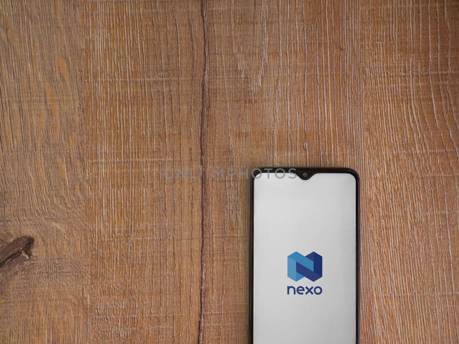 Lod, Israel - July 16,2023: Nexo app launch screen on smartphone on wooden background. Top view flat lay with copy space.