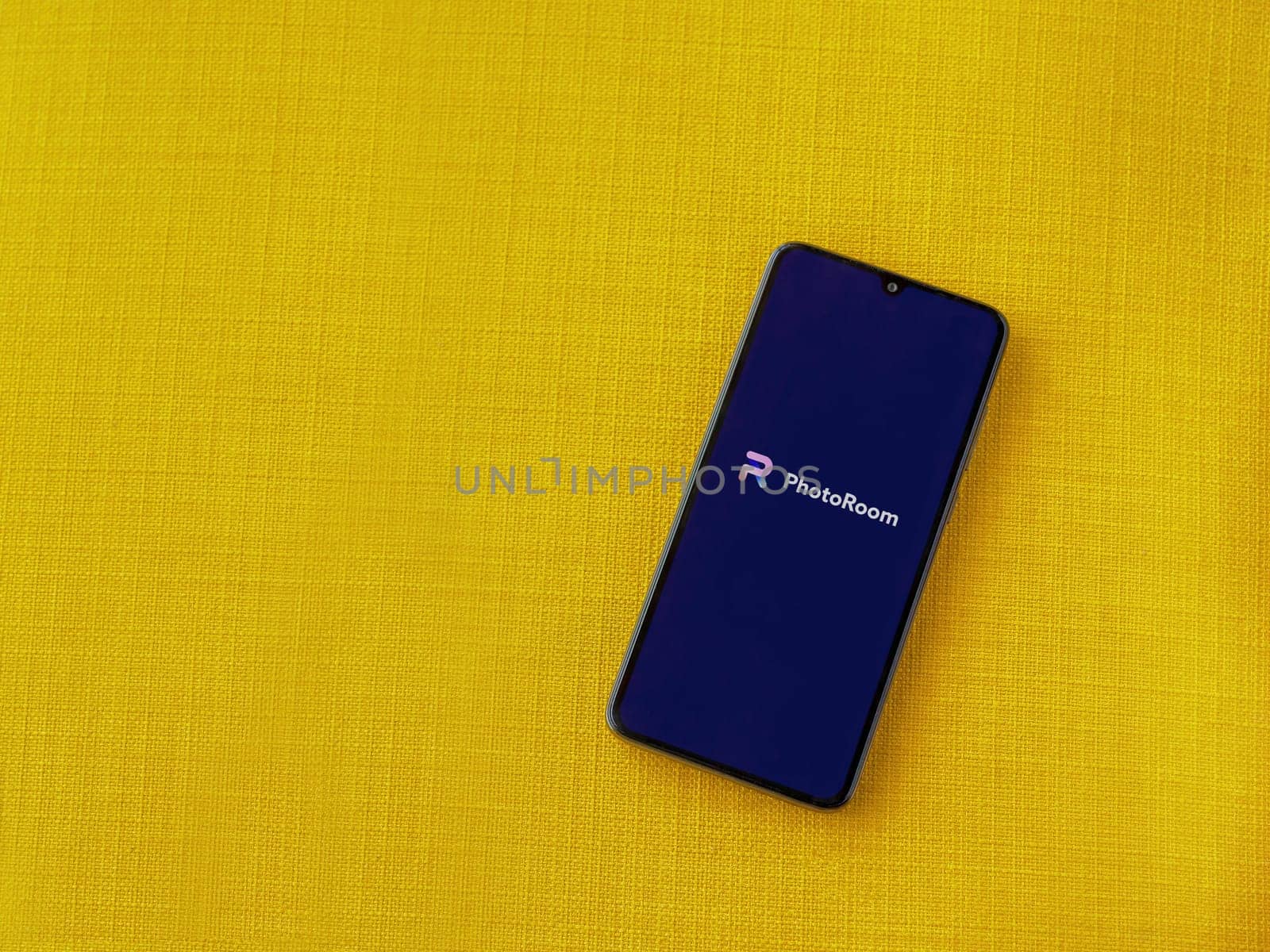 Lod, Israel - July 16,2023: PhotoRoom Studio Photo Editor app launch screen on smartphone on yellow fabric background.. Top view flat lay with copy space.