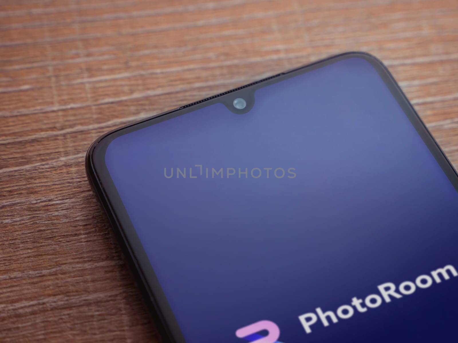 Lod, Israel - July 16,2023: PhotoRoom Studio Photo Editor app launch screen on smartphone on wooden background.. Top view flat lay with copy space.