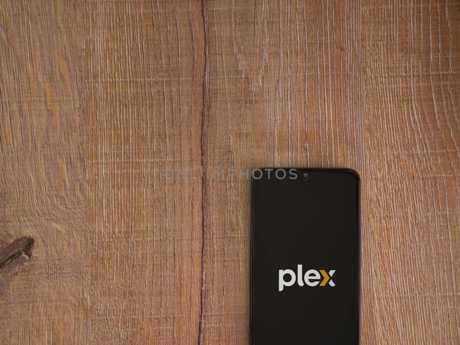 Lod, Israel - July 16,2023: Plex app launch screen on smartphone on wooden background. Top view flat lay with copy space.