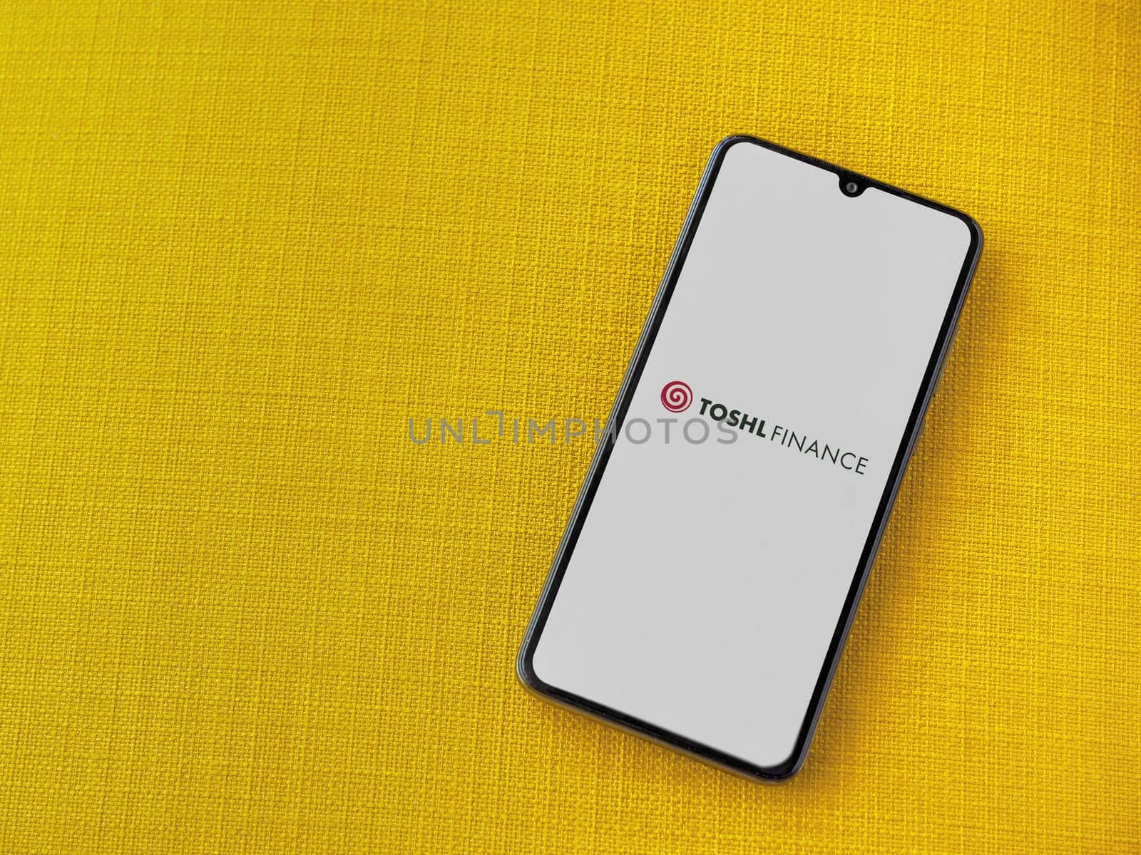 Lod, Israel - July 16,2023: Toshl Finance app launch screen on smartphone on yellow fabric background. Top view flat lay with copy space.