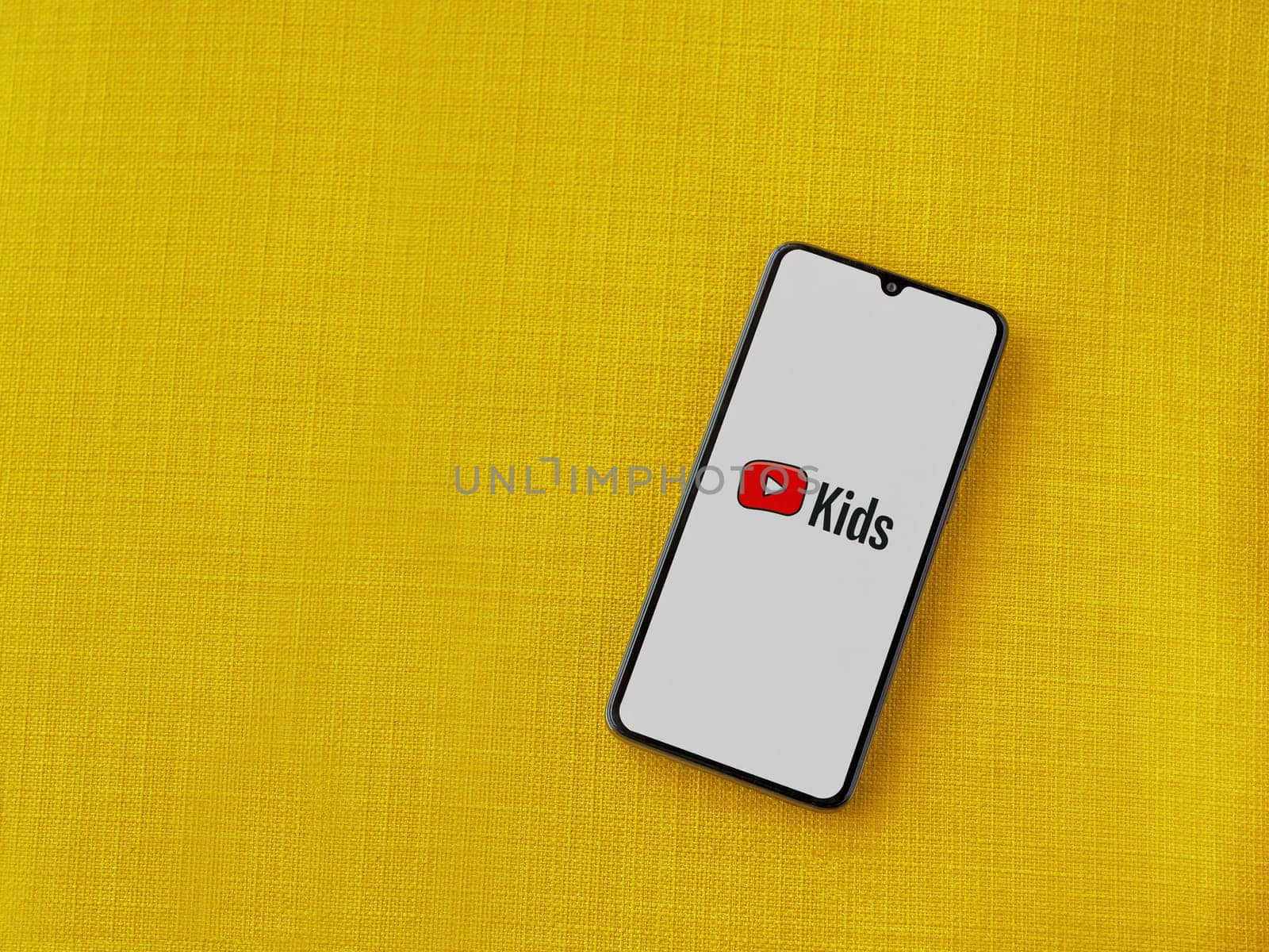 Lod, Israel - July 16,2023: YouTube Kids app launch screen on smartphone on yellow fabric background. Top view flat lay with copy space.