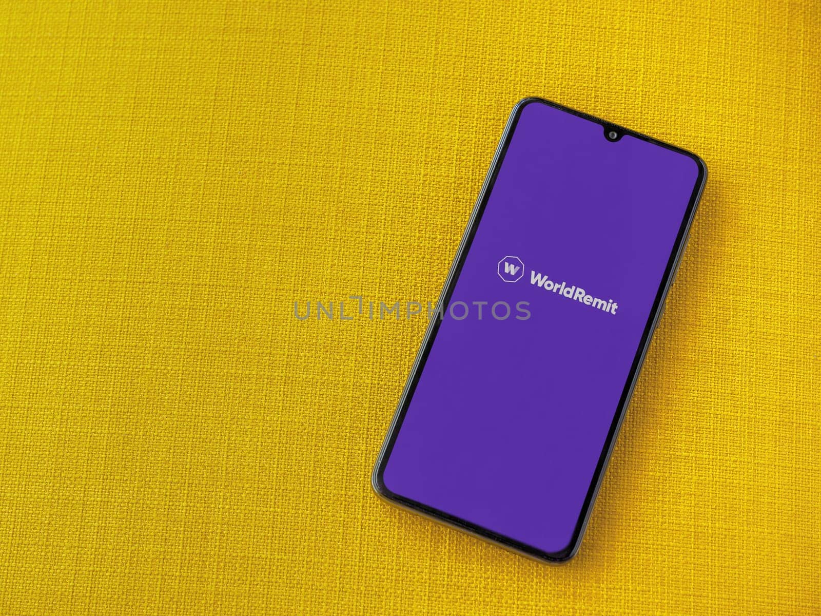 Lod, Israel - July 16,2023: WorldRemit app launch screen on smartphone on yellow fabric background. Top view flat lay with copy space.