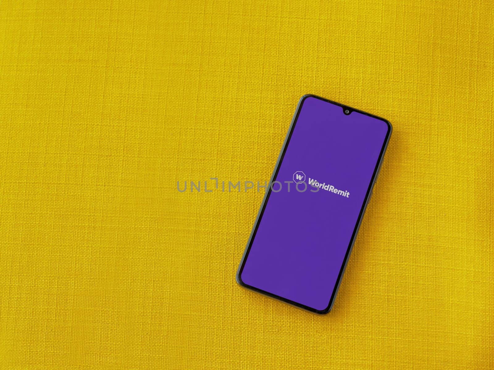 Lod, Israel - July 16,2023: WorldRemit app launch screen on smartphone on yellow fabric background. Top view flat lay with copy space.
