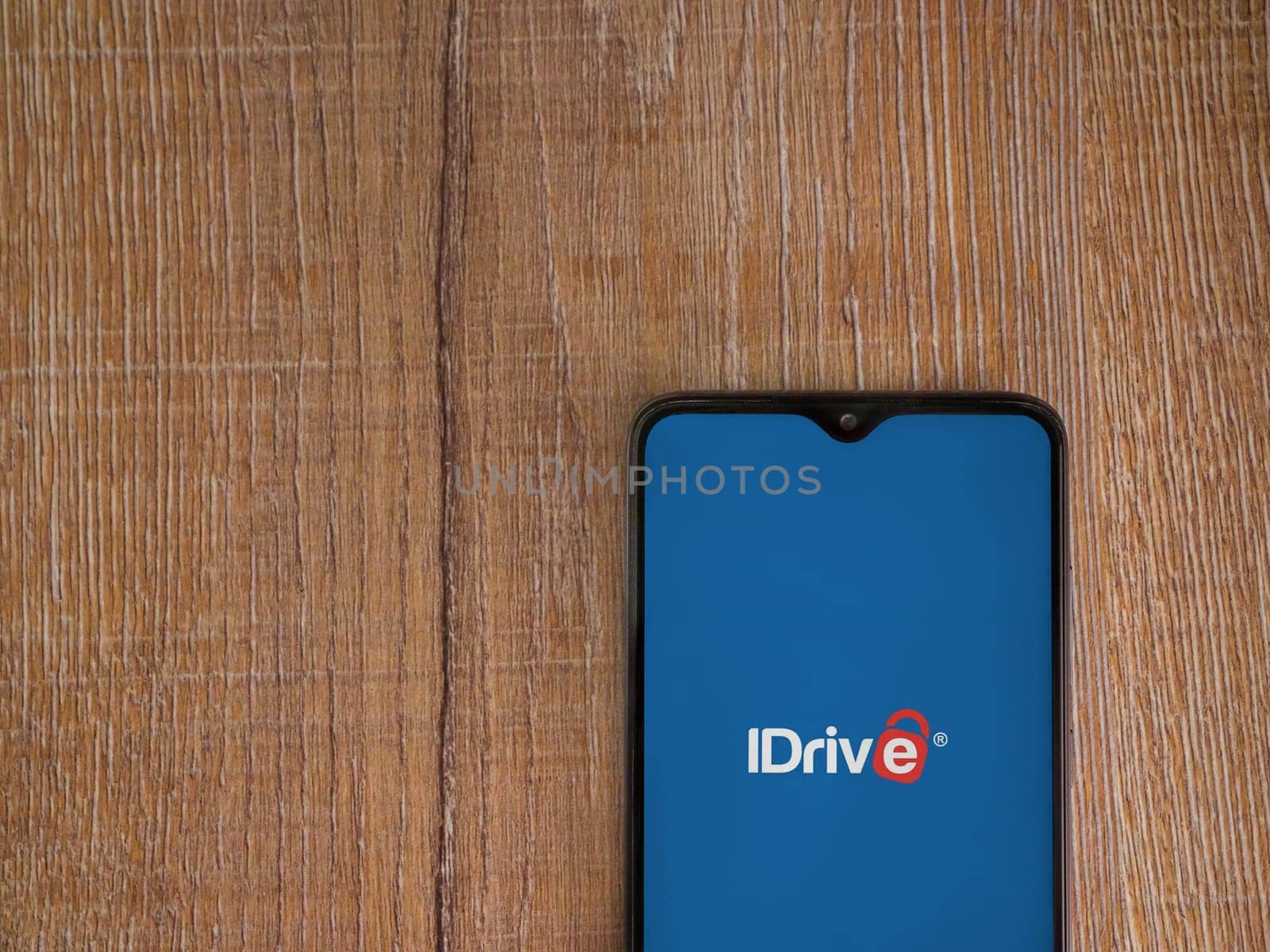Lod, Israel - July 16,2023: IDrive Online Backup app launch screen on smartphone on wooden background. Top view flat lay with copy space.