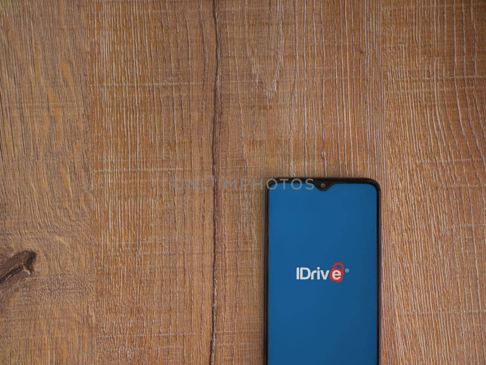 Lod, Israel - July 16,2023: IDrive Online Backup app launch screen on smartphone on wooden background. Top view flat lay with copy space.
