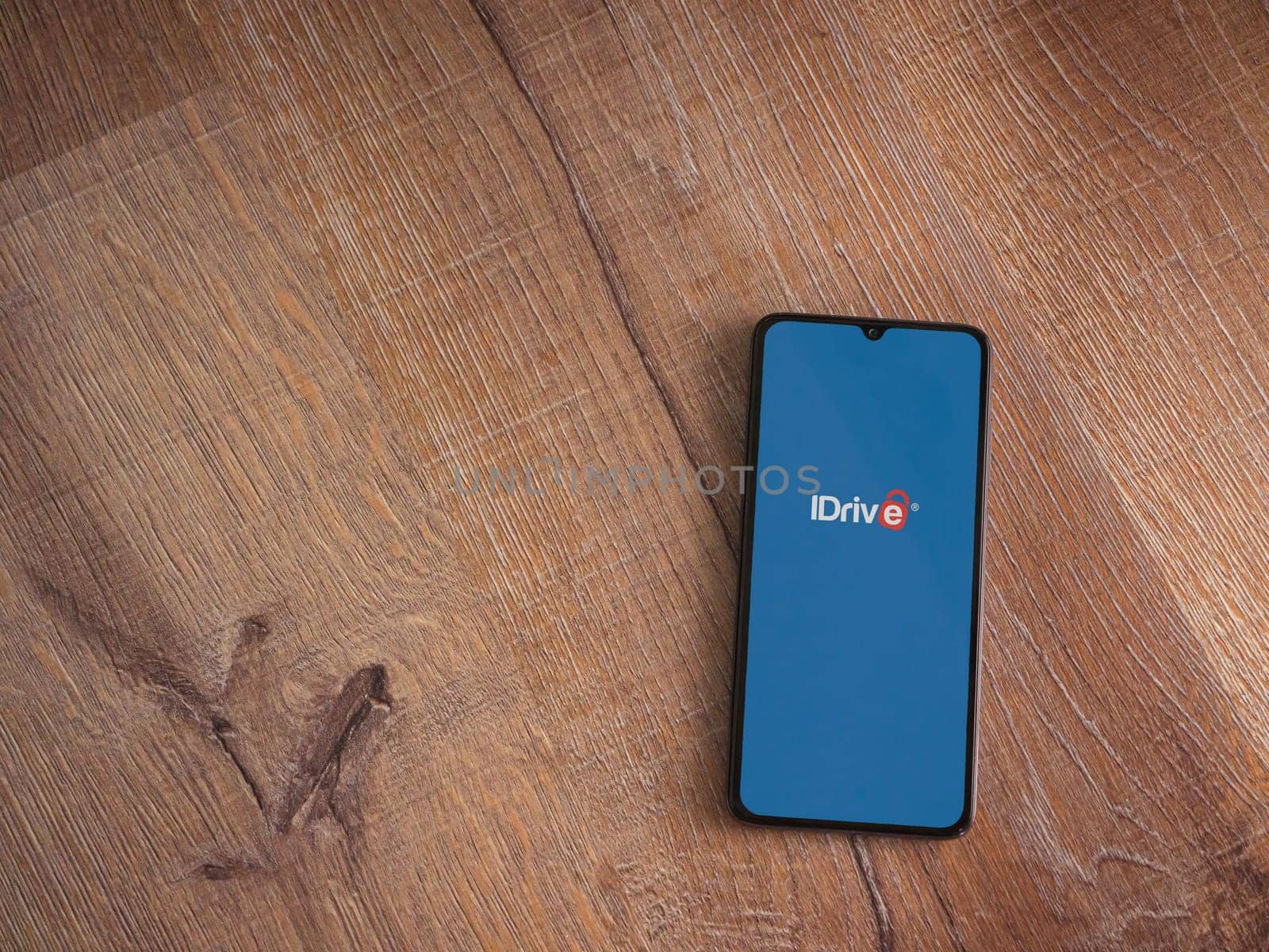Lod, Israel - July 16,2023: IDrive Online Backup app launch screen on smartphone on wooden background. Top view flat lay with copy space.