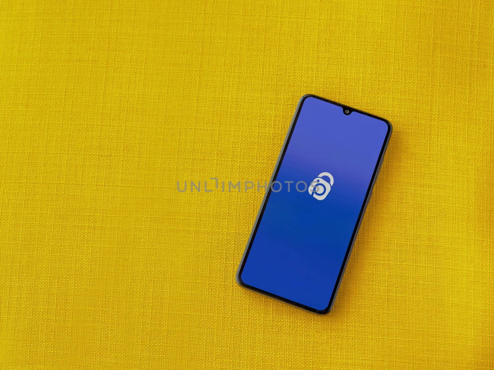 Lod, Israel - July 16,2023: IDrive Photo Backup app launch screen on smartphone on yellow fabric background. Top view flat lay with copy space.