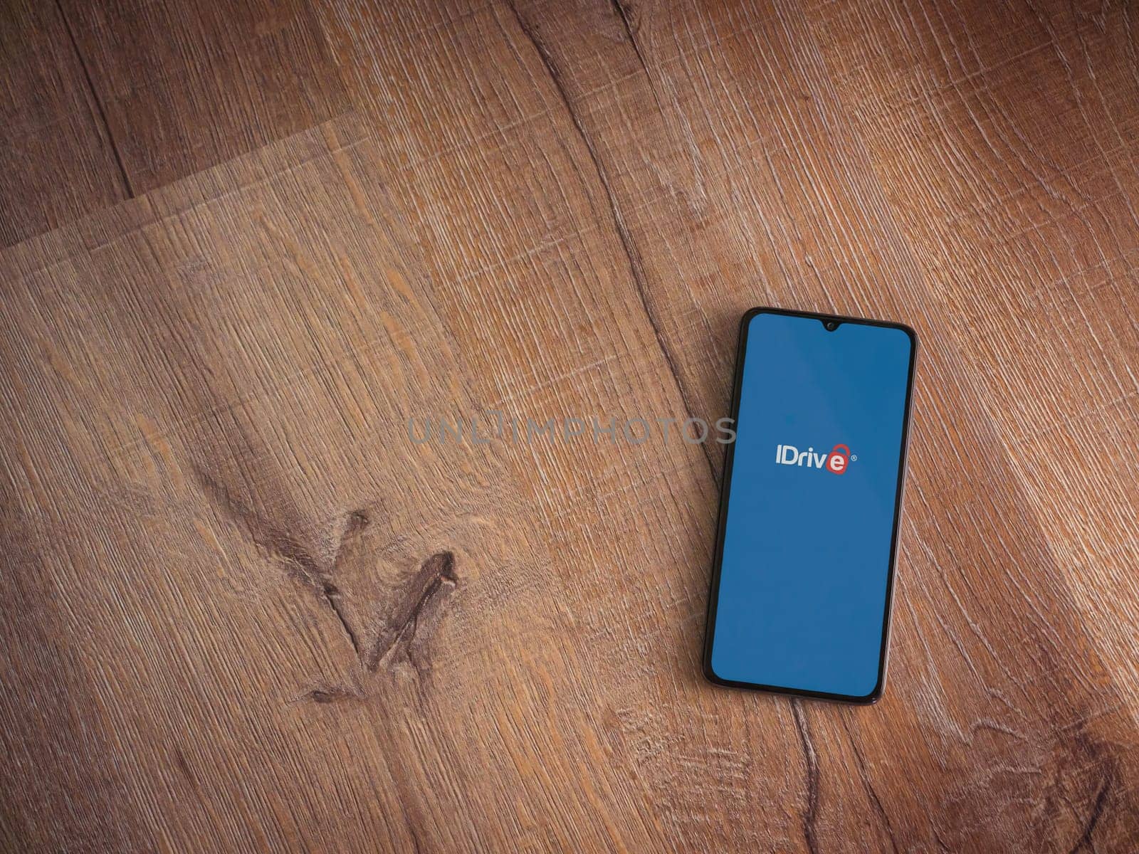 Lod, Israel - July 16,2023: IDrive Online Backup app launch screen on smartphone on wooden background. Top view flat lay with copy space.