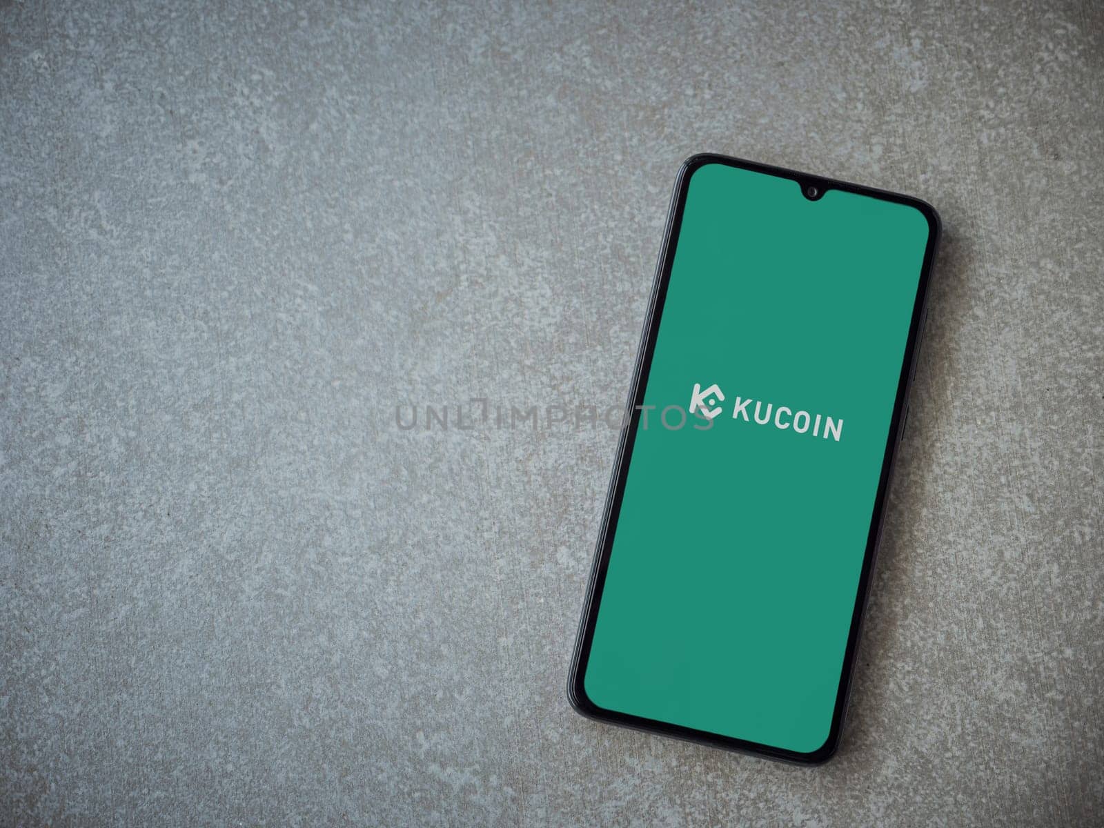 Lod, Israel - July 16,2023: KuCoin app launch screen on smartphone on ceramic stone background. Top view flat lay with copy space.