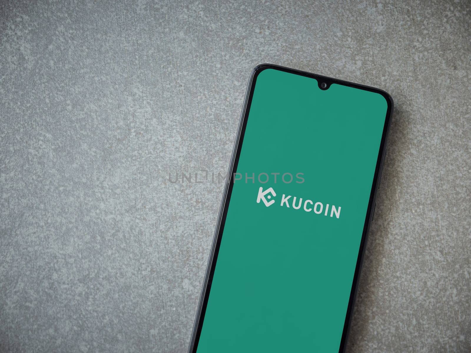 Lod, Israel - July 16,2023: KuCoin app launch screen on smartphone on ceramic stone background. Top view flat lay with copy space.