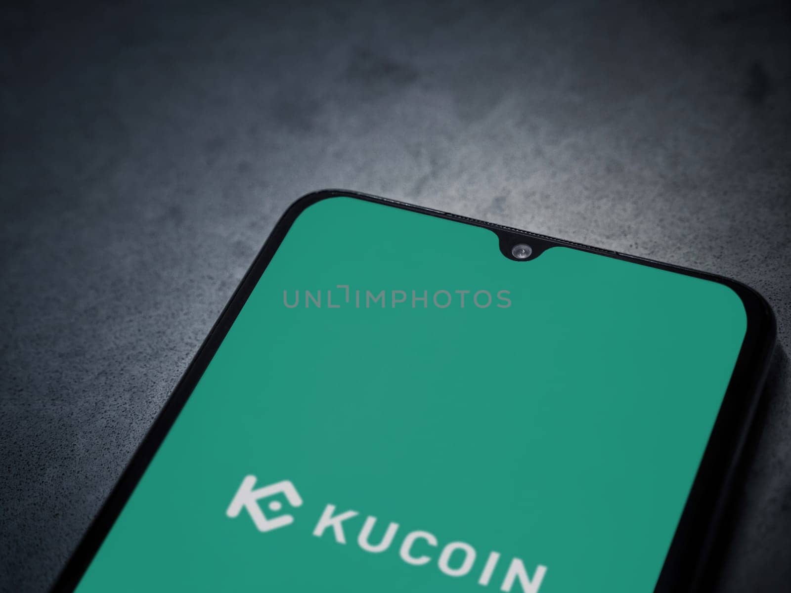 Lod, Israel - July 16,2023: KuCoin app launch screen on smartphone on dark marble stone background. Top view flat lay with copy space.