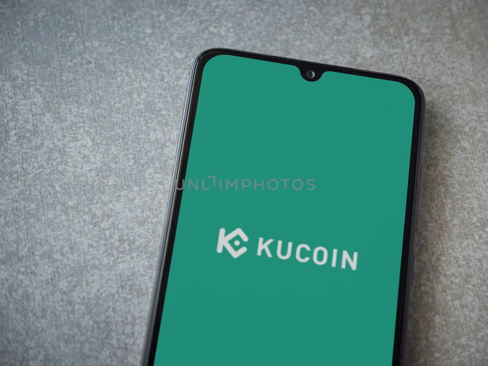 Lod, Israel - July 16,2023: KuCoin app launch screen on smartphone on ceramic stone background. Top view flat lay with copy space.