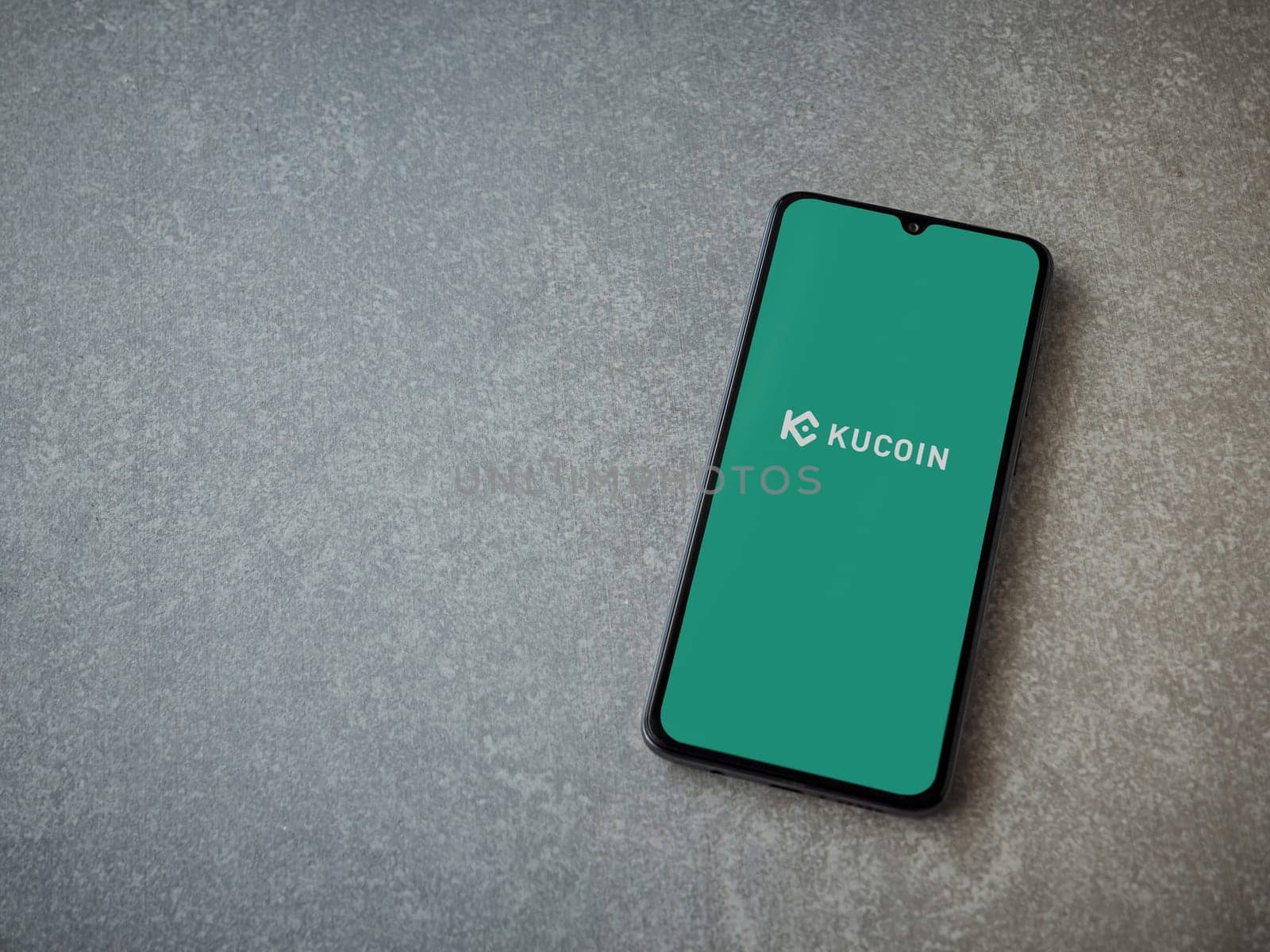 Lod, Israel - July 16,2023: KuCoin app launch screen on smartphone on ceramic stone background. Top view flat lay with copy space.