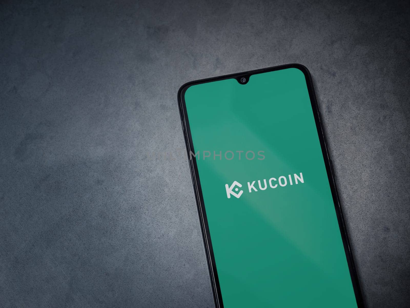 Lod, Israel - July 16,2023: KuCoin app launch screen on smartphone on dark marble stone background. Top view flat lay with copy space.