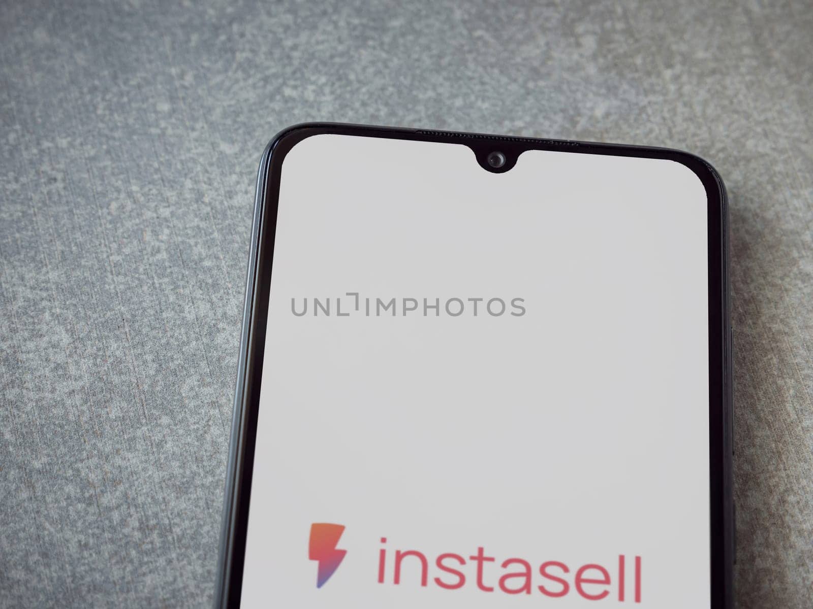 Lod, Israel - July 16,2023: Instasell app launch screen on smartphone on ceramic stone background. Top view flat lay with copy space.