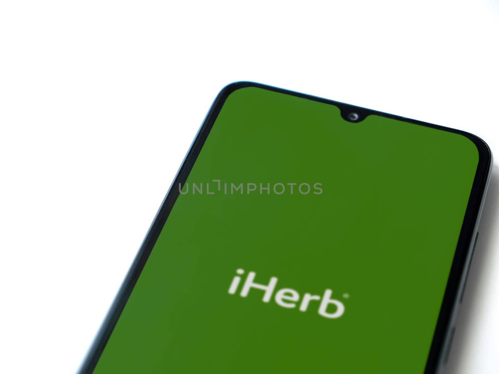 Lod, Israel - July 16,2023: iHerb app launch screen on smartphone on white background. Top view flat lay with copy space.