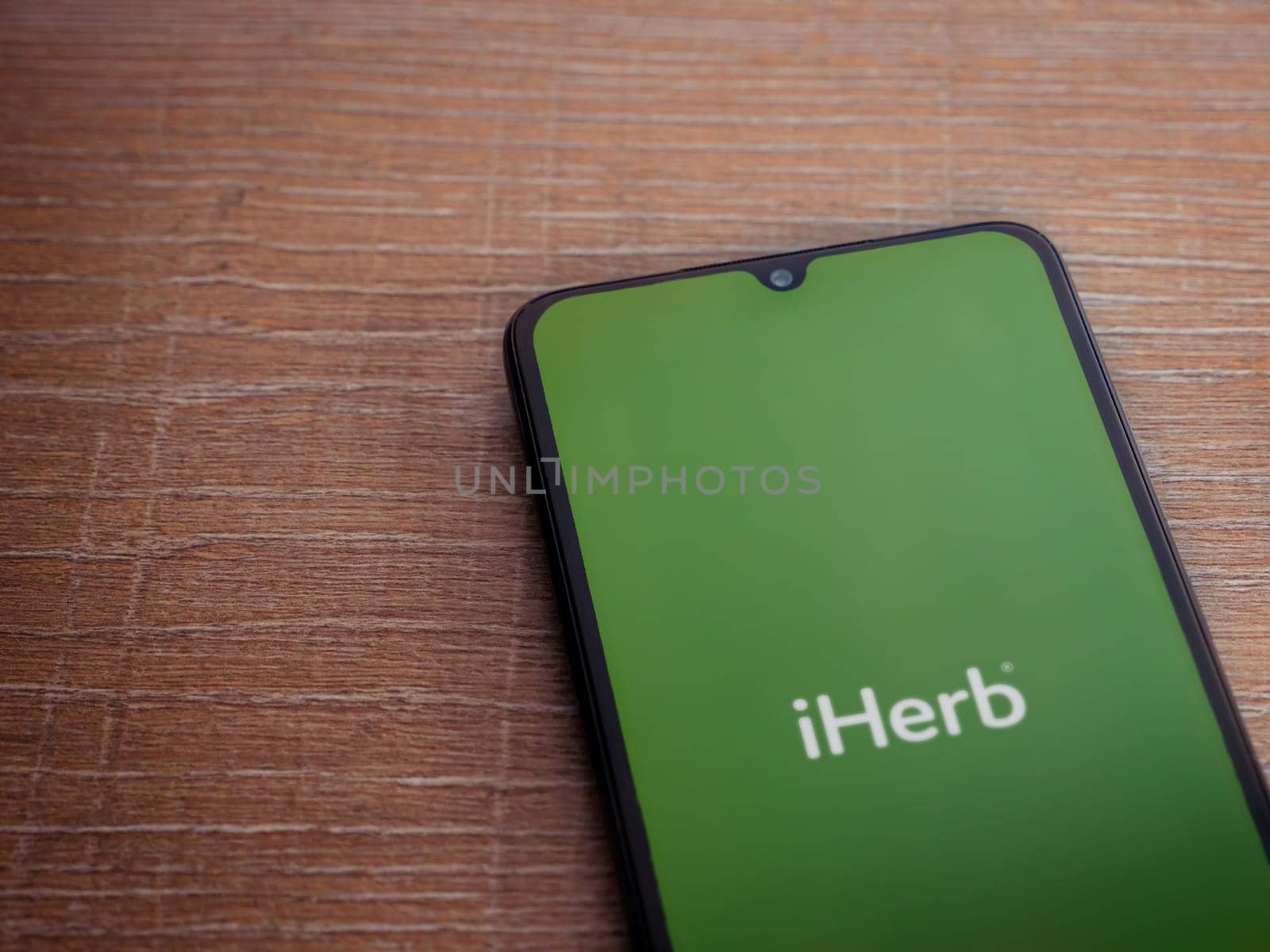 Lod, Israel - July 16,2023: iHerb app launch screen on smartphone on wooden background. Top view flat lay with copy space.