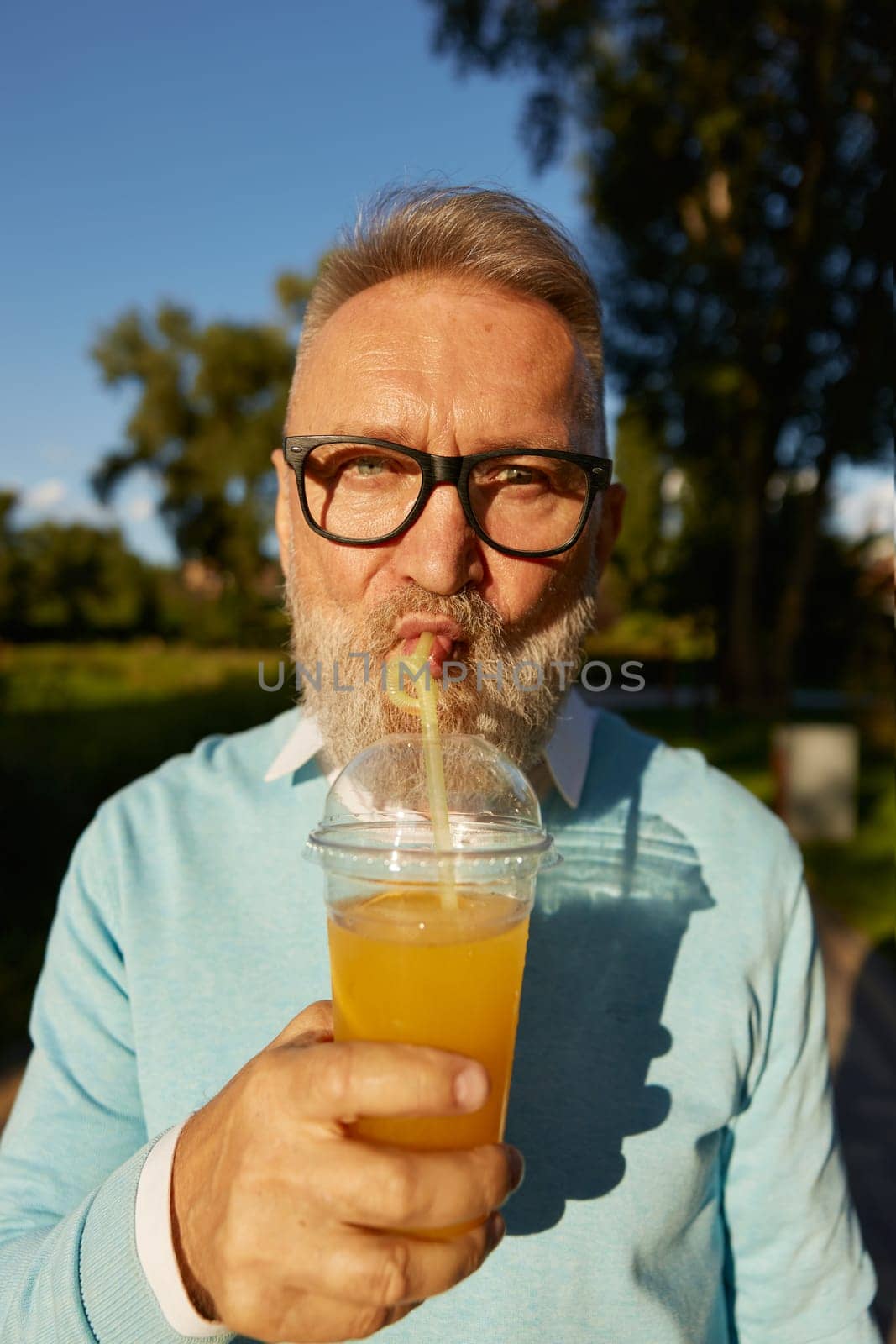 Closeup face portrait of old senior man drinking cool refreshment cocktail from straw in takeaway couple. Hot summer day and active walk of retired male in public park