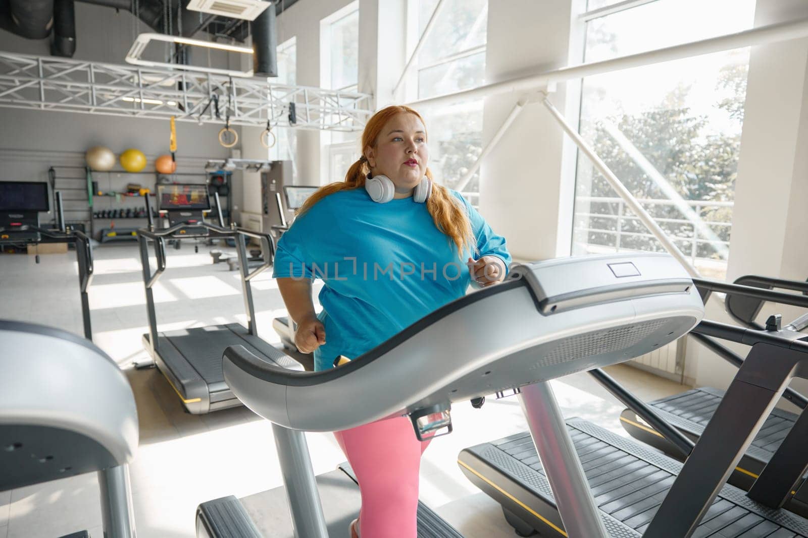 Active obese woman running on treadmill track enjoying cardio exercise for calorie burning. Sportive challenge for slimming