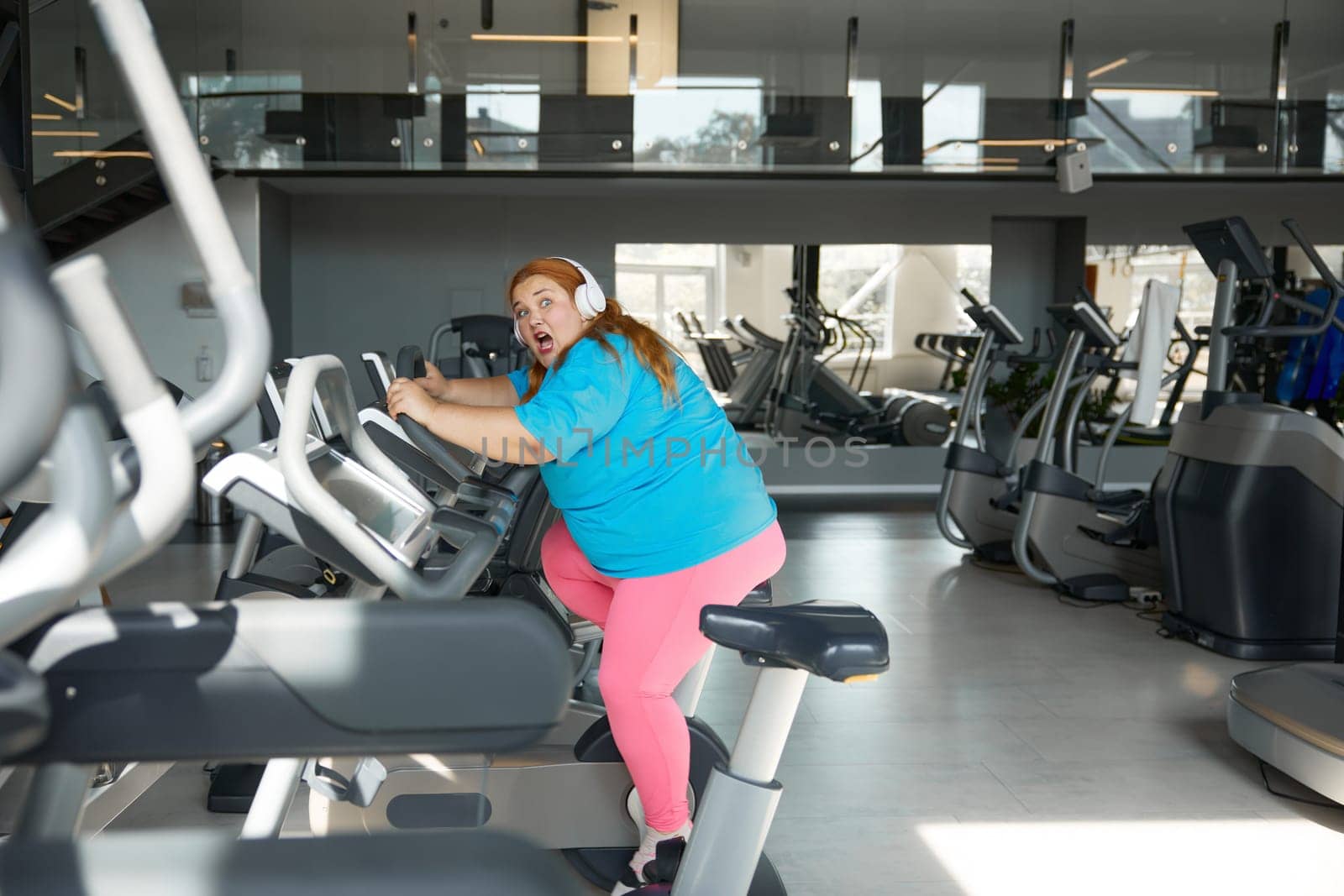 Crazy motivated overweight woman riding fast on stationary bike in gym. Fitness class for obese people concept