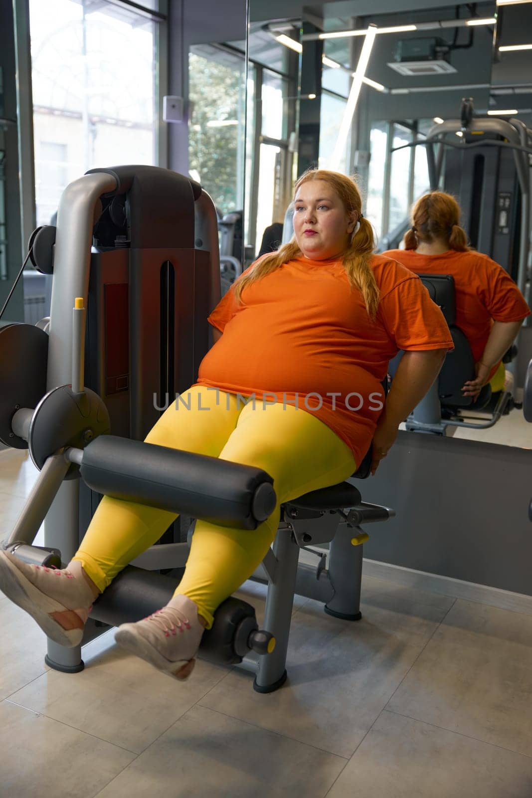 Beautiful chubby girl sportive outfit training at gym doing legs pump exercises on sports equipment