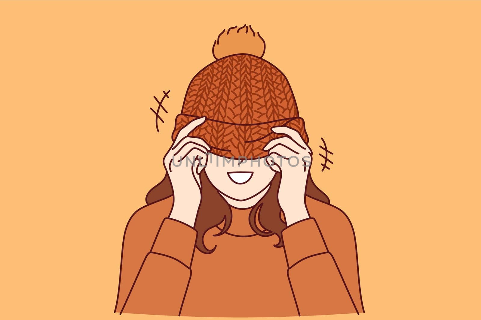 Woman covers face with knitted hat with pompom and smiles standing in warm sweater. Happy girl rejoices at onset of winter or autumn cold weather and puts on handmade hat given by loved one