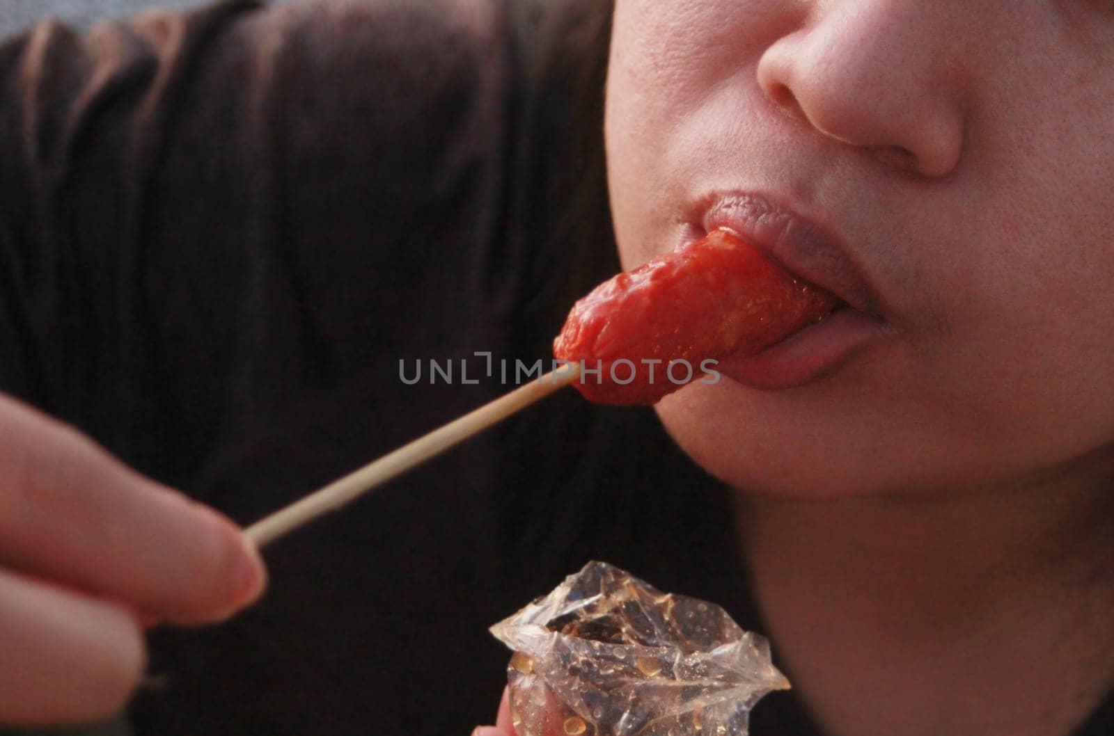 Woman happily eating sausage on gray blurred background