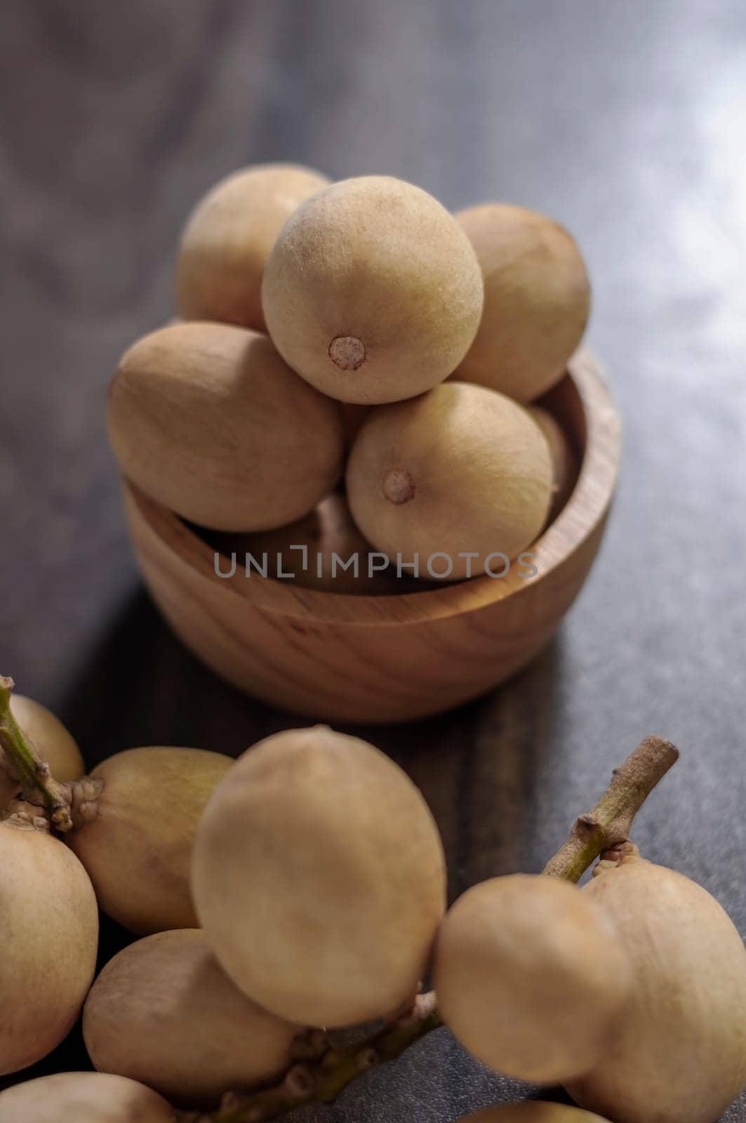 Langsat Longkong is a fruit found in the forests of tropical countries in Asia. And it is a fruit with a delicious aroma that is popular in Thailand, Malaysia, Singapore, Indonesia, Laos and Vietnam. Langsat Longkong is placed in a wooden cup on a dark wooden plank table with a blurred background.