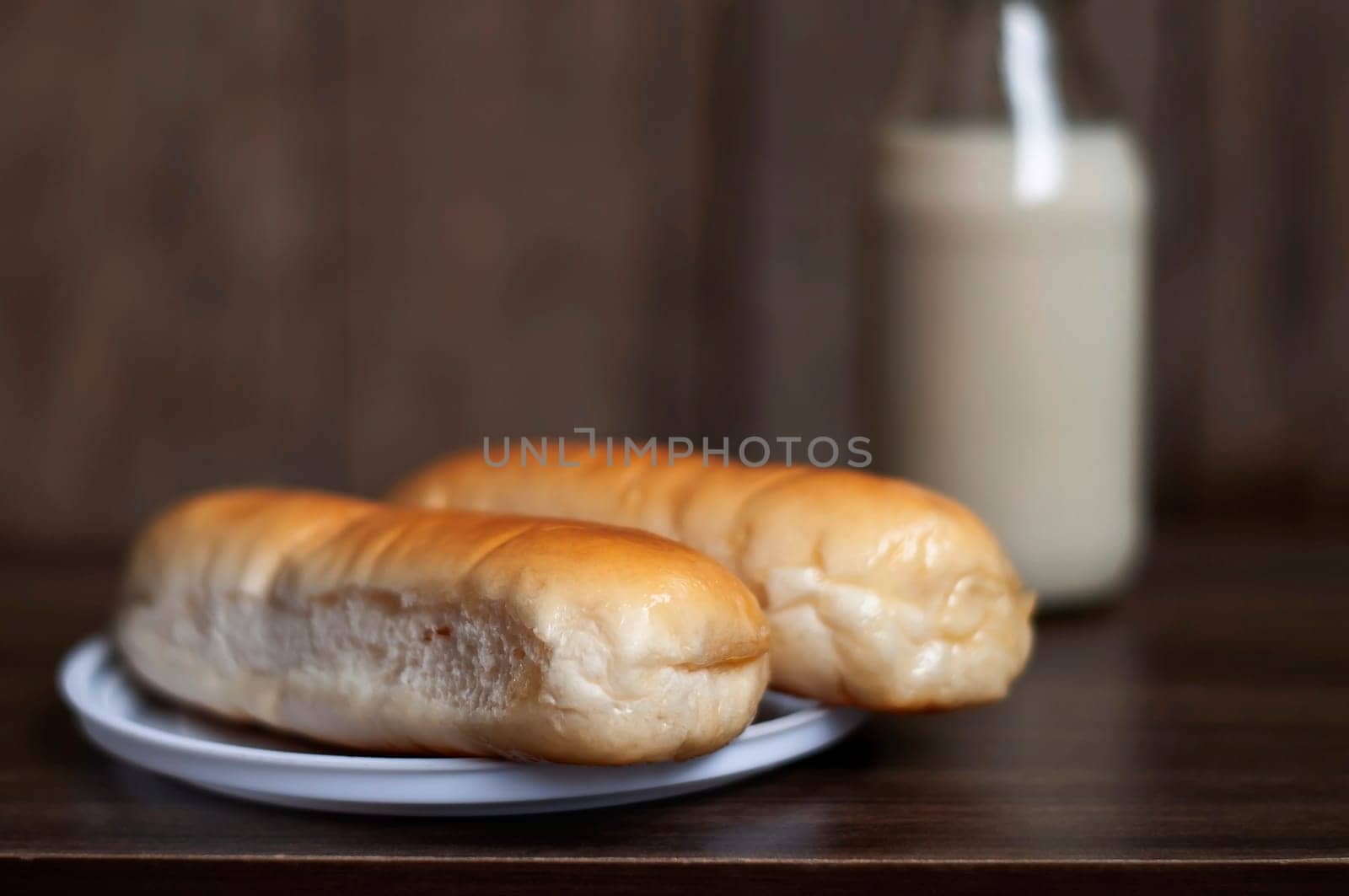 Bread on a white plate sits on a wooden board table with milk in a bottle behind it with copy space. Blurred background