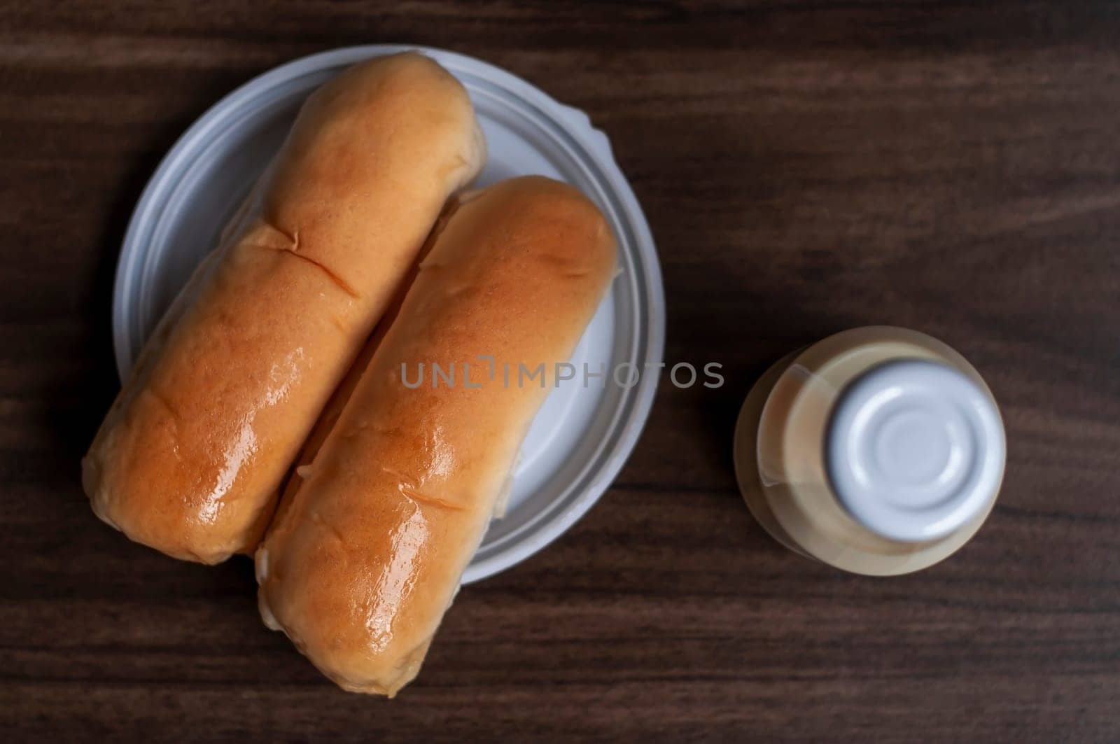 Bread on a white plate sits on a wooden board table with milk in a bottle behind it with copy space. Blurred background