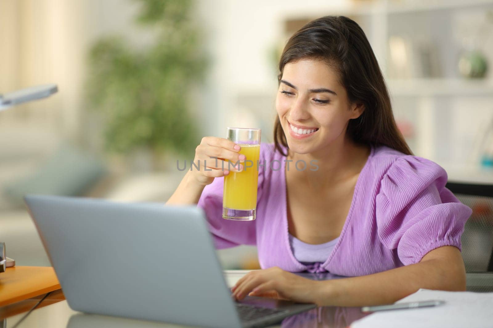Happy student drinking orange juice e-learning at home