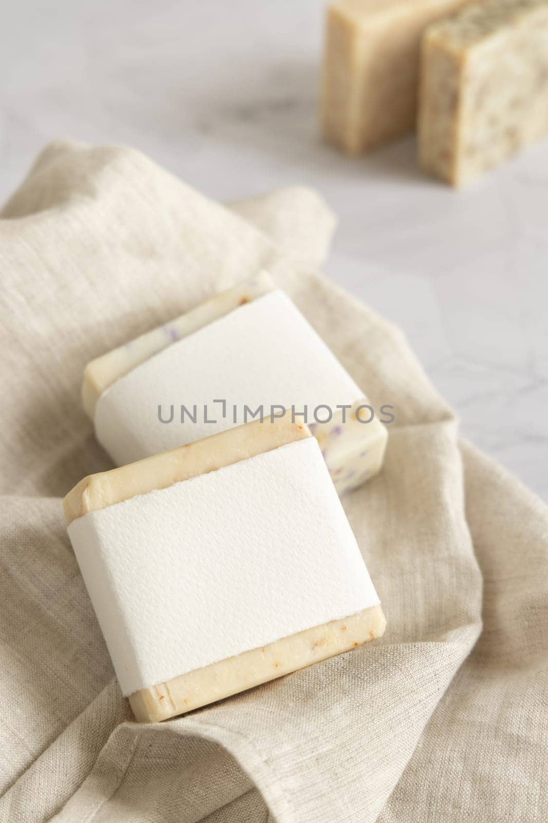 Beige handmade soap bars with blank label on linen towel close up, mockup, copy space. Natural herbal products for face and body care