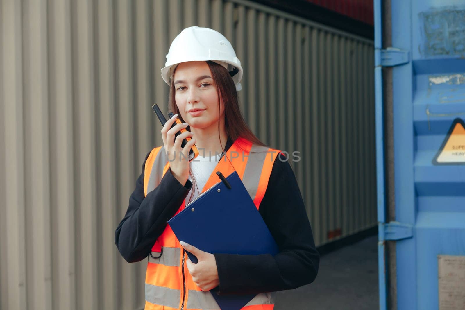 Female Foreman using walkie talkie radio and clip folder, control loading containers box