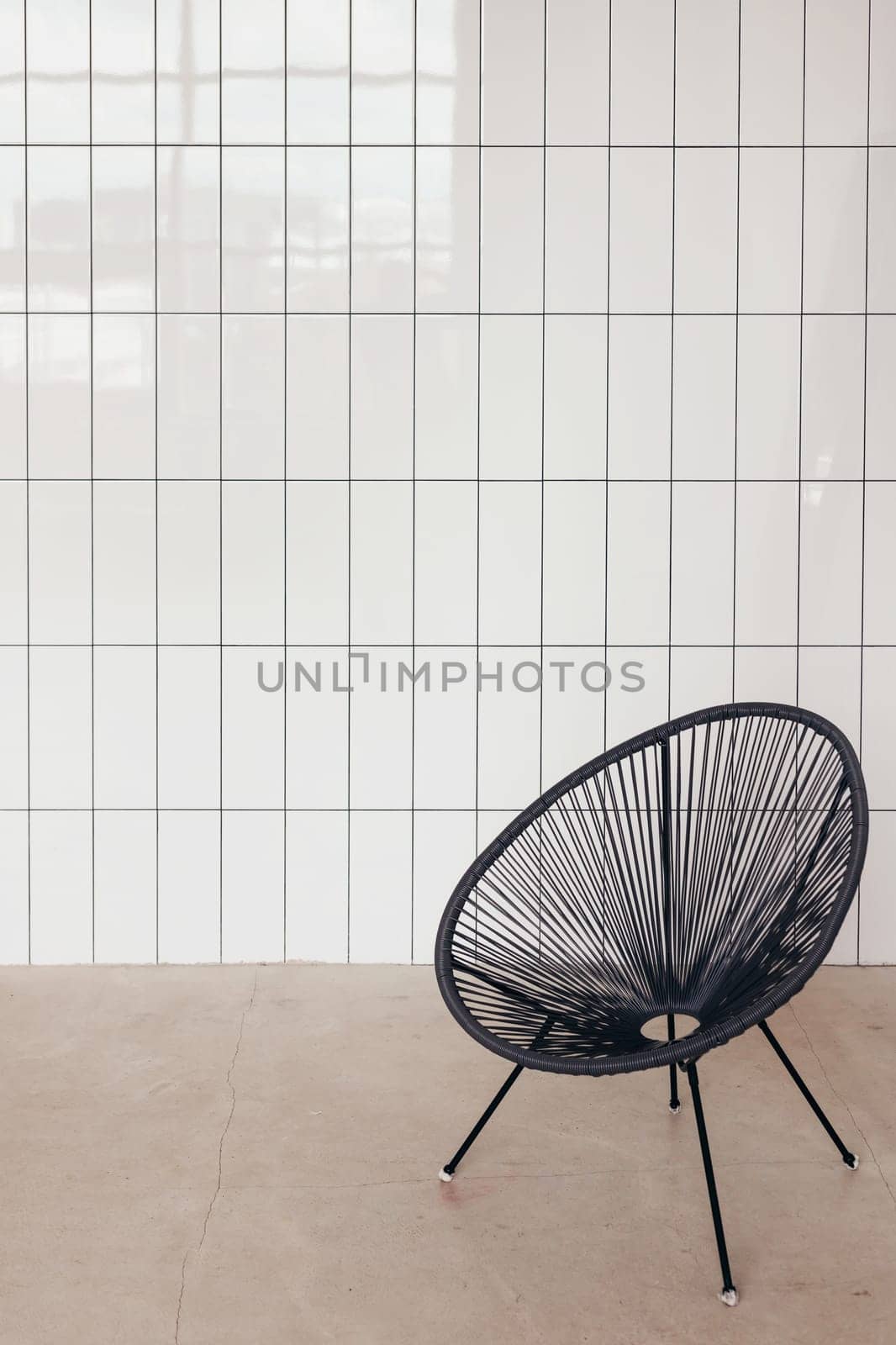 Wicker string chair against white ceramic tile wall. Minimal interior.